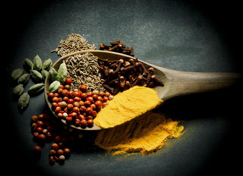 A wooden spoon holding a blend of whole and ground spices